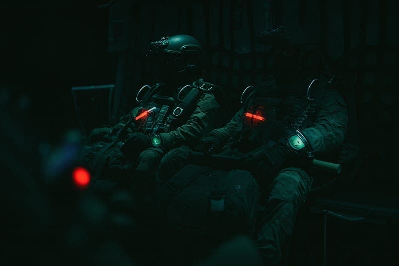 Special Forces soldiers sitting inside military transport aircraft in full tactical gear, listening to mission briefing before HALO jump deployment behind enemy lines